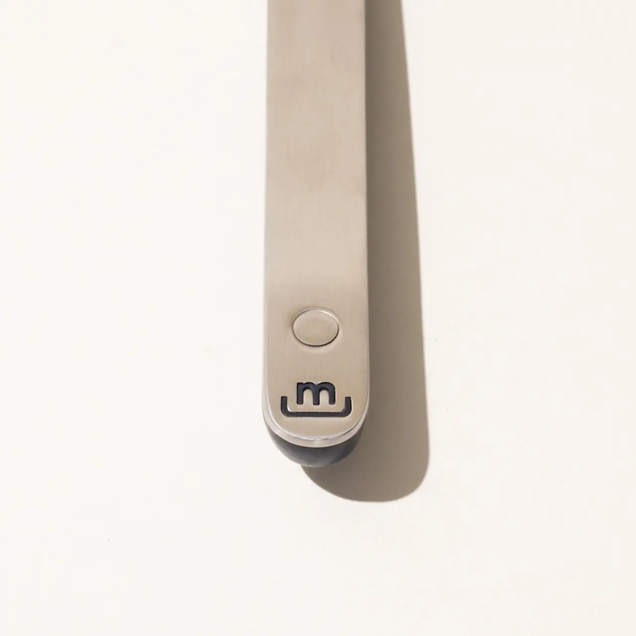 A close-up of a sleek electronic device with a single button and a logo resembling the letter "m" on a plain background.