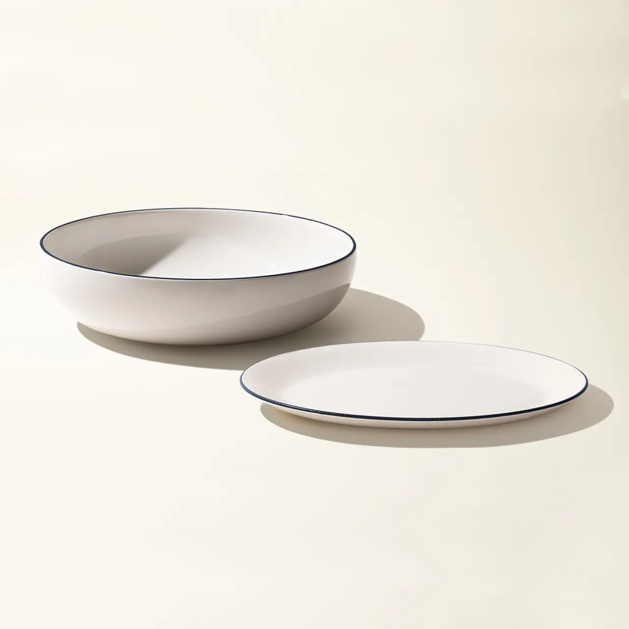 A bowl and a plate with simple designs are placed on a light surface, casting soft shadows.