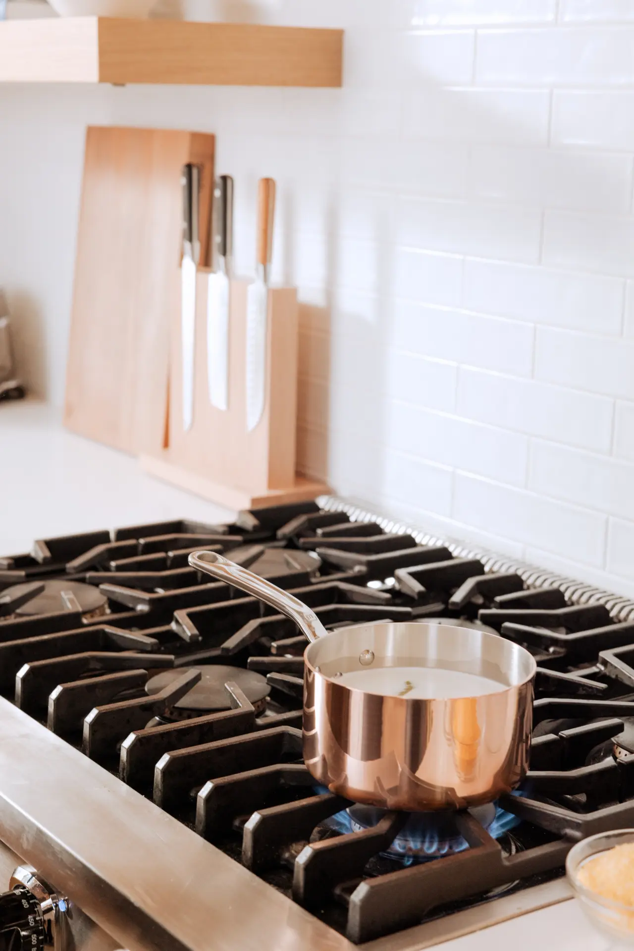 A stainless steel pot sits on a gas stove burner with a set of knives mounted on a wooden block in the background.