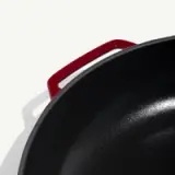 A close-up view of a cast iron pot with a glossy black interior and a red handle on one side.