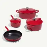 A set of red cookware consisting of two pots with lids, a saucepan with a lid, and a skillet on a light background.