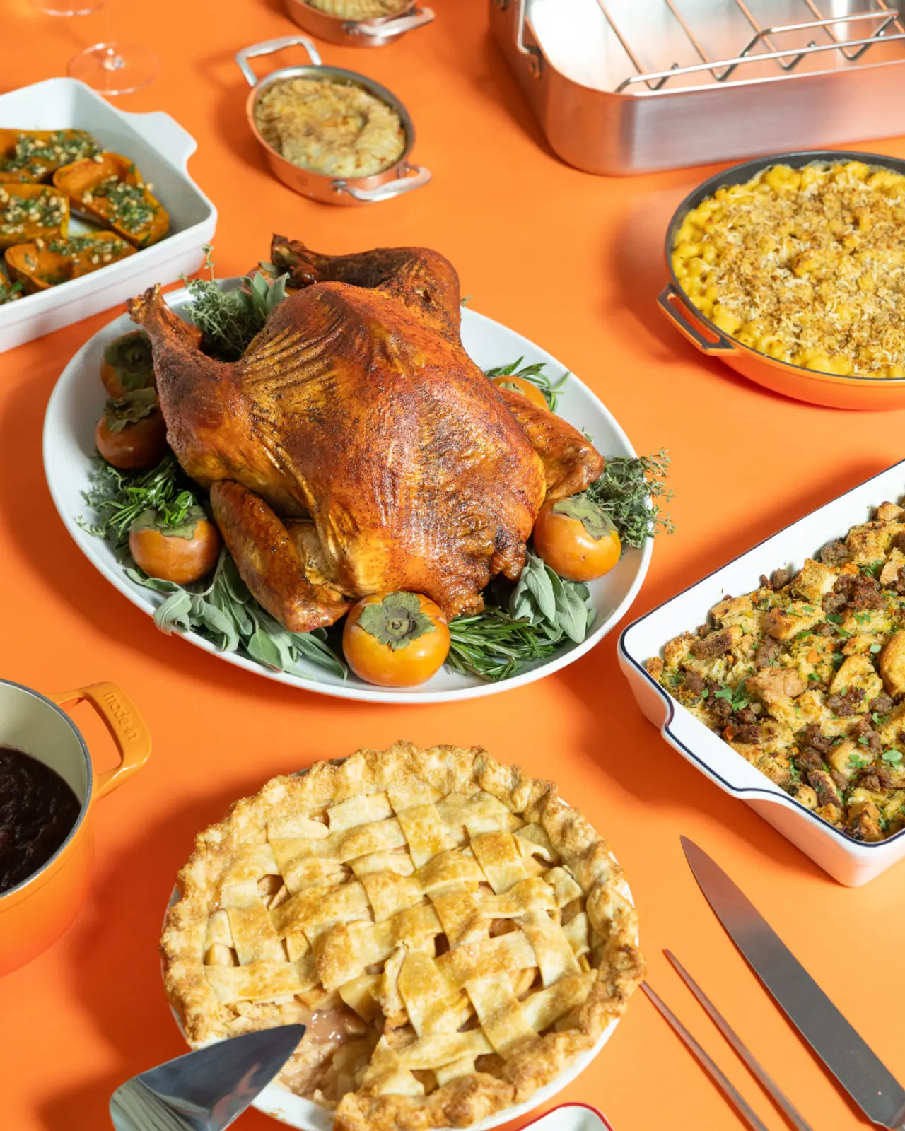 A festive table setting features a golden brown turkey centerpiece surrounded by various dishes such as stuffing, pie, and vegetables, suggesting a Thanksgiving meal.