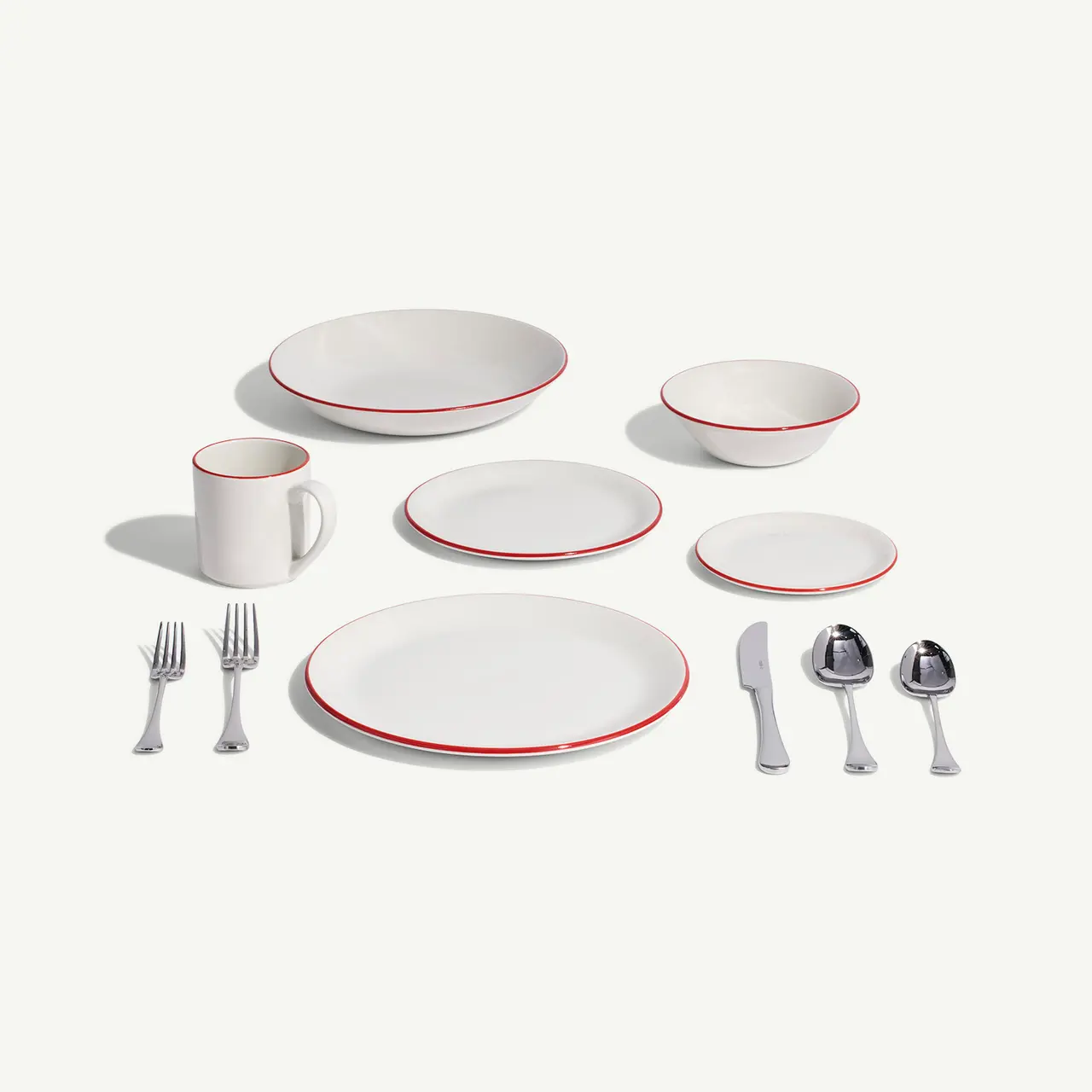 A neatly arranged dinnerware set with red trim, including plates, bowls, a mug, and cutlery, on a plain background.