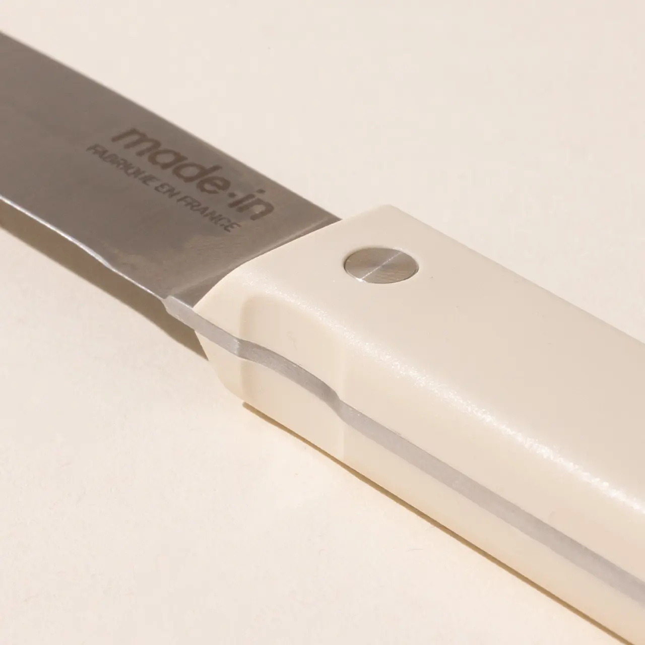 Close-up of a kitchen knife with a stainless steel blade and a white handle, marked with the text "made in" and branding or model information.