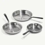 Three different-sized stainless steel frying pans with black handles are arranged by size on a light background.