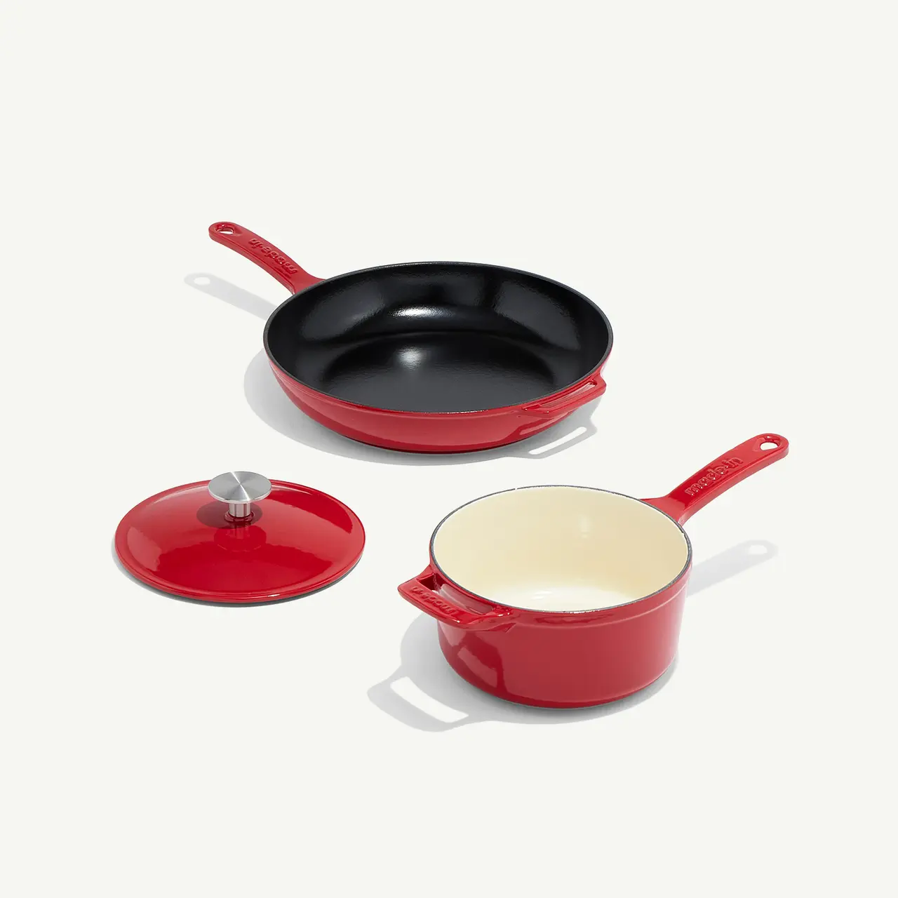 A set of red cookware consisting of a frying pan, saucepan with a lid, and a pot on a white background.