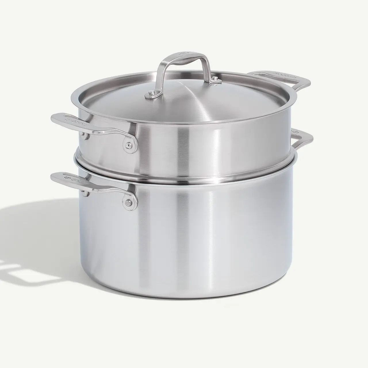 A stainless steel double boiler with a lid on a neutral background.