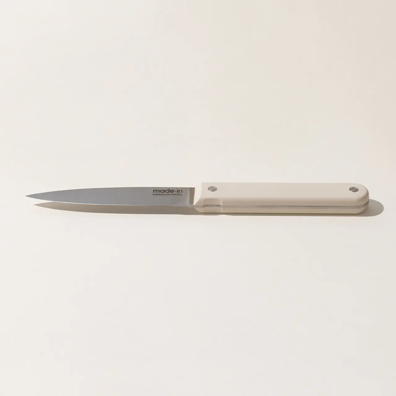 A simple kitchen knife with a white handle and silver blade, with the text "made in" on the blade, isolated against a plain background.