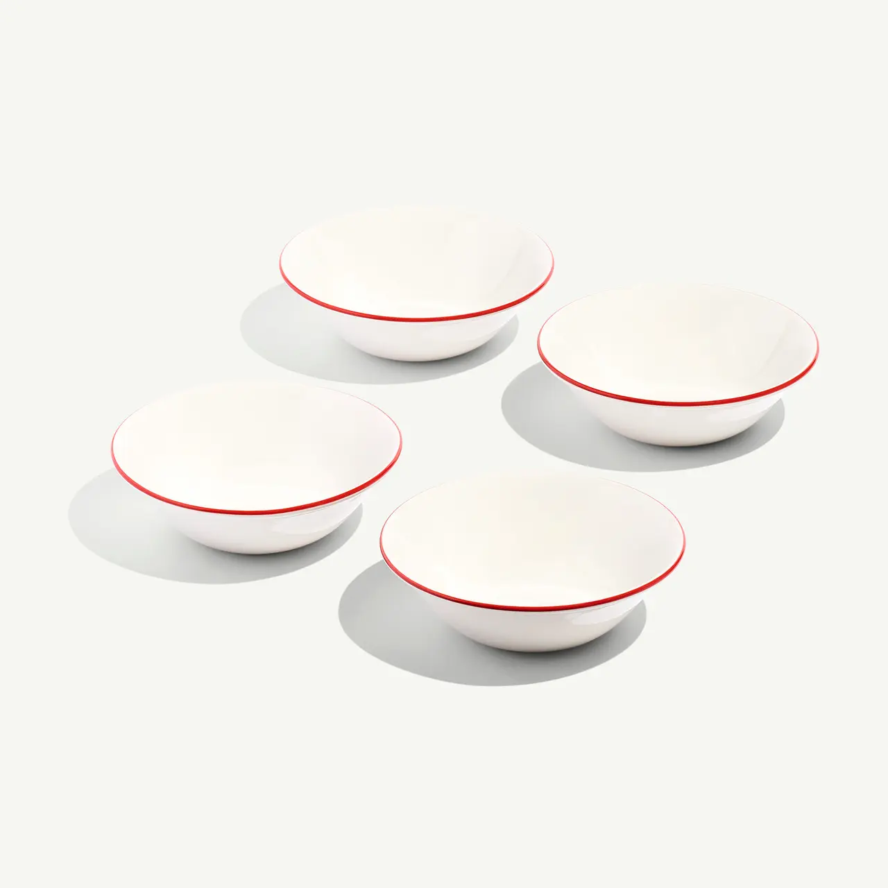 Four white bowls with red rims are arranged on a pale surface.