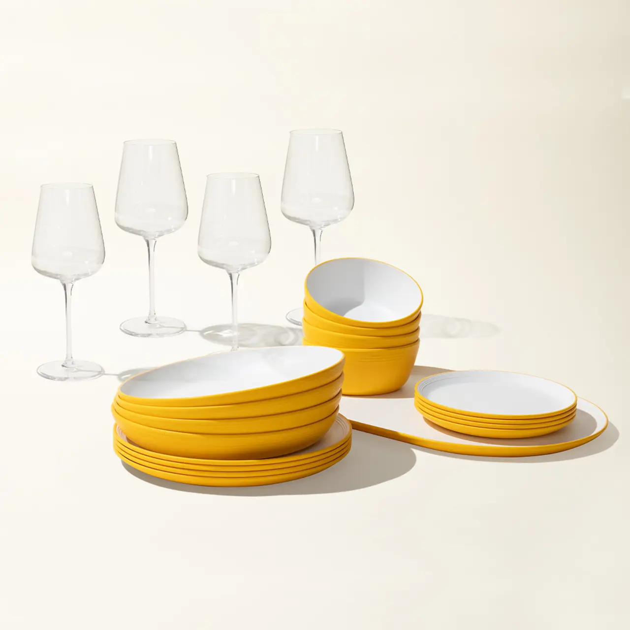 A neatly arranged set of yellow dishes and clear wine glasses casts soft shadows on a light background.