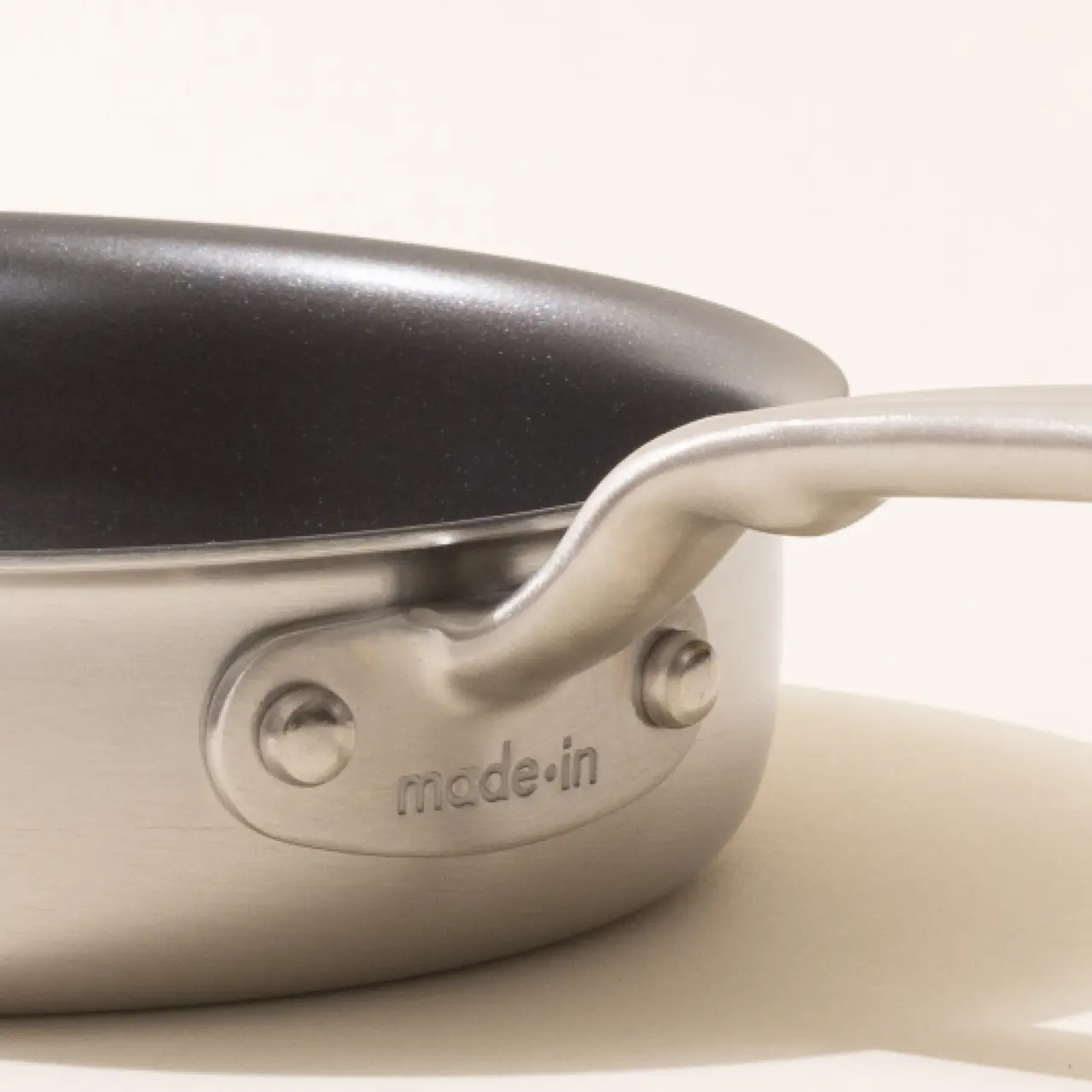 A close-up of a stainless steel saucepan with a black non-stick coating inside and the word "madein" embossed on the handle.