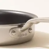 A close-up of a stainless steel saucepan with a black non-stick coating inside and the word "madein" embossed on the handle.