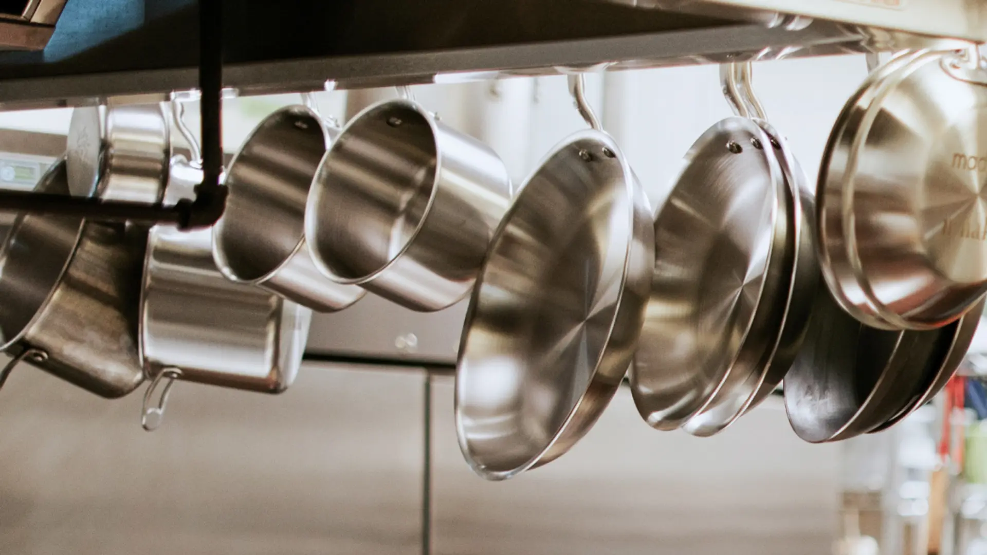 An array of stainless steel pots and pans hangs neatly from a kitchen rack, reflecting the light softly.