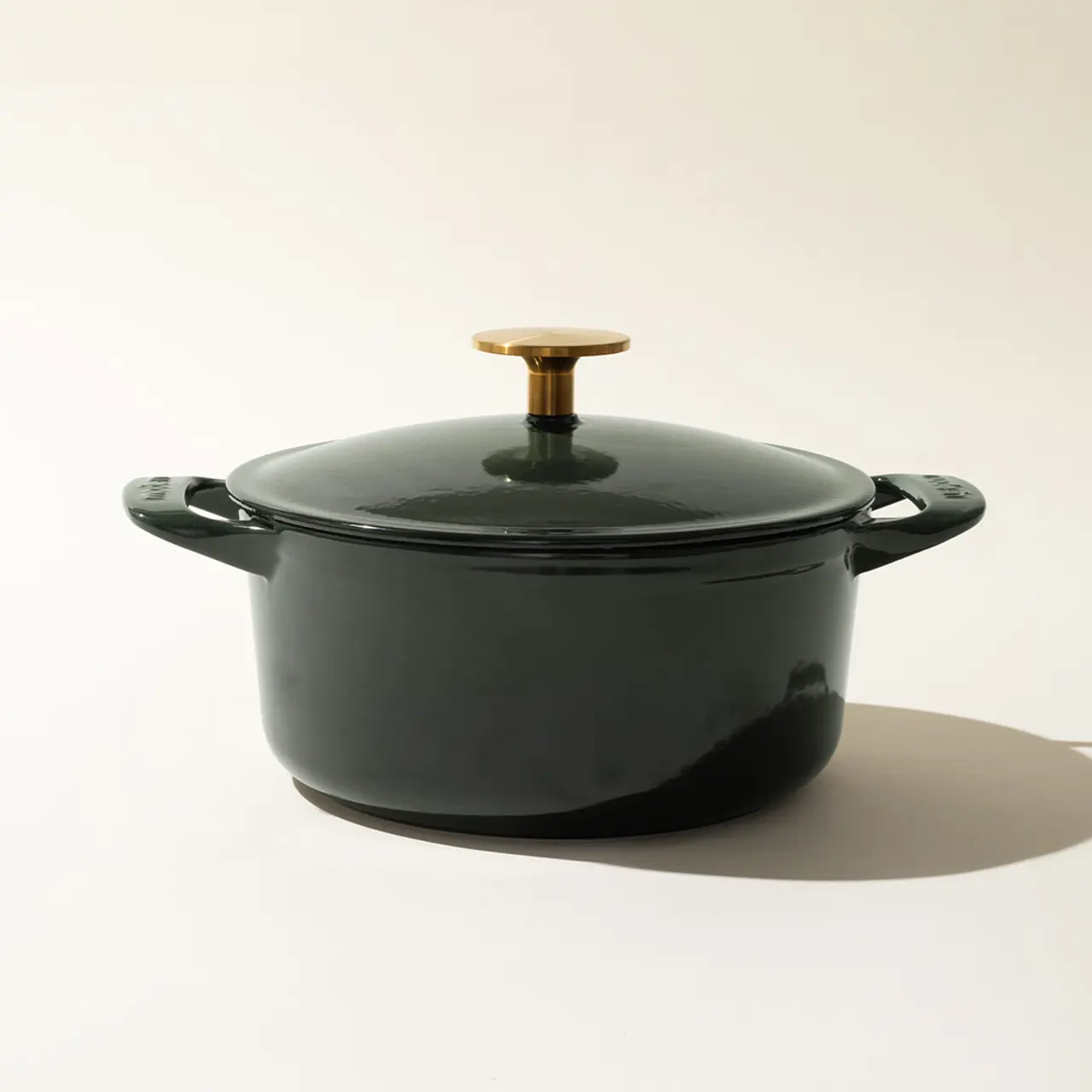 A dark-colored cooking pot with a lid featuring a contrasting gold-colored handle, set against a neutral background.