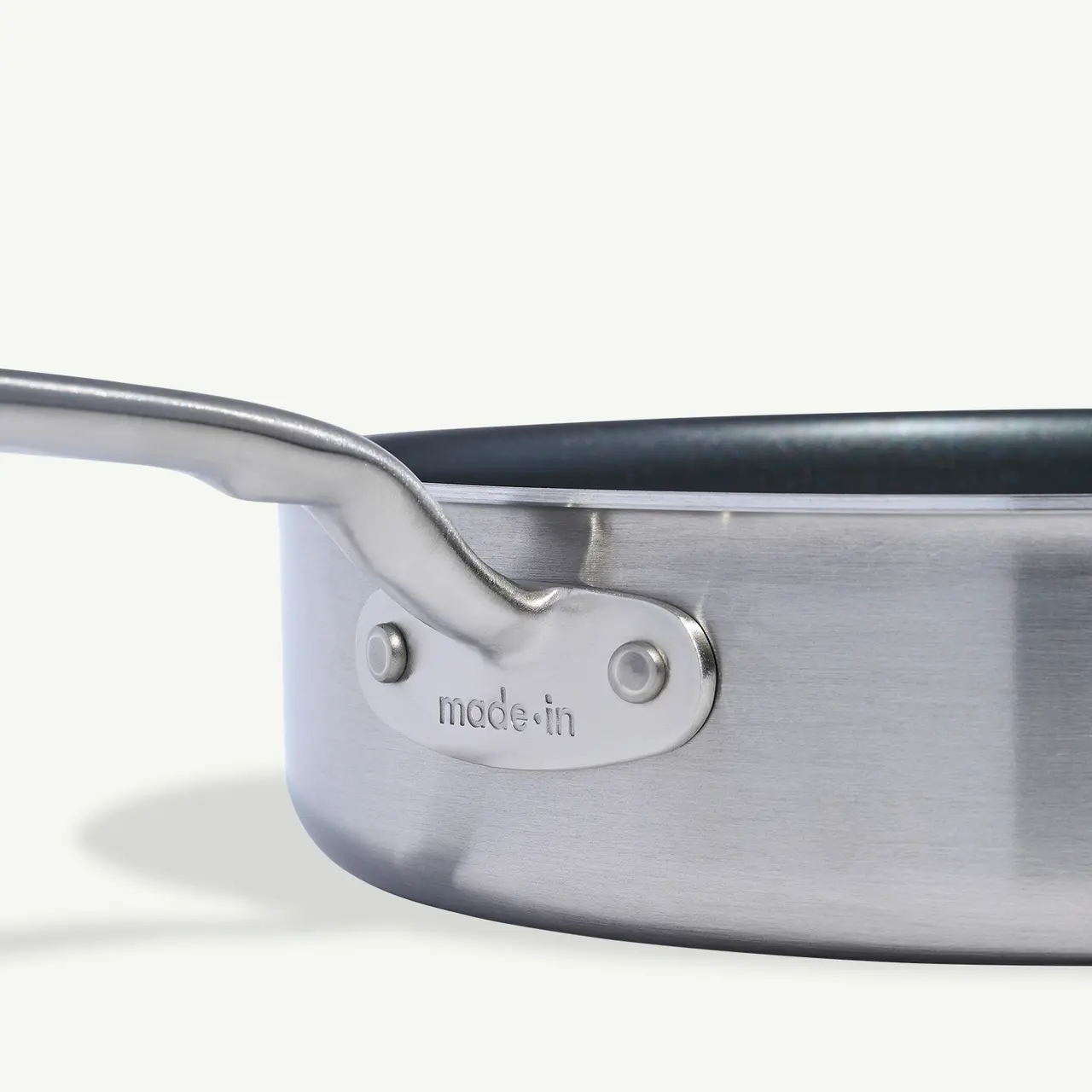 A close-up view of a stainless steel pan with the text "made in" stamped near the joint of the handle.