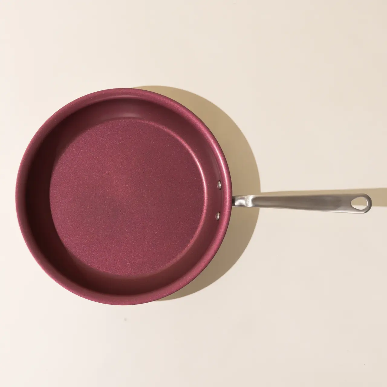 A new maroon non-stick frying pan with a stainless steel handle, photographed from above on a beige surface.