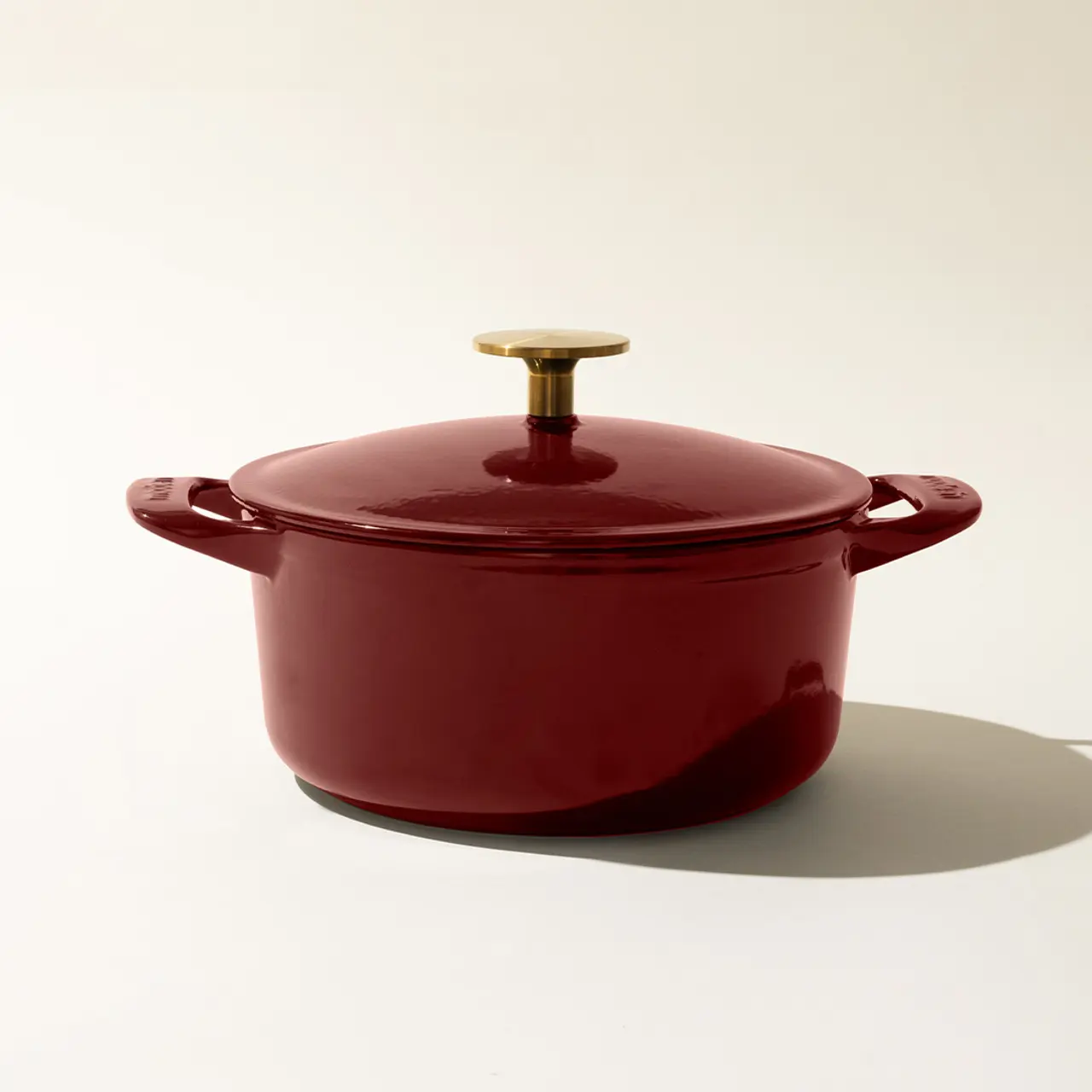 A red enameled cast iron Dutch oven with a gold-tone knob on the lid, centered against a light background.