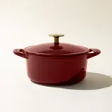 A red enameled cast iron Dutch oven with a gold-tone knob on the lid, centered against a light background.