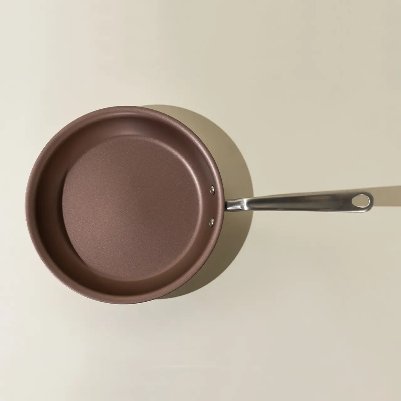 A top-down view of a brown pan with a long silver handle resting on a light surface.