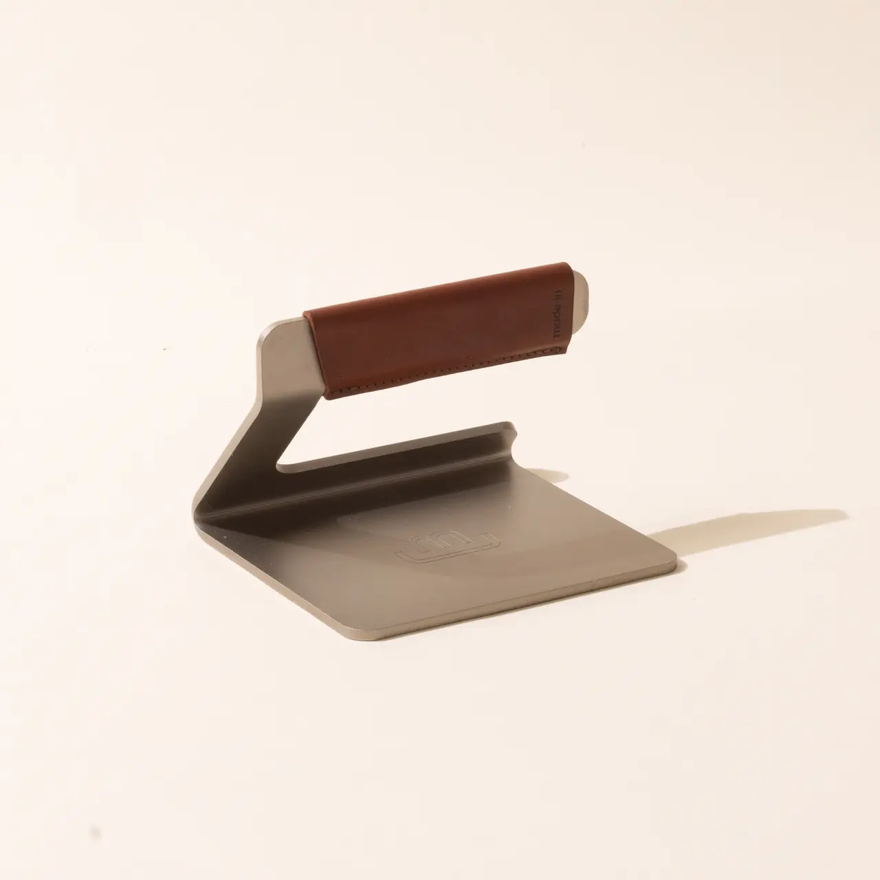 A minimalist metal bookend with a brown leather accent stands on a light background, casting a soft shadow.