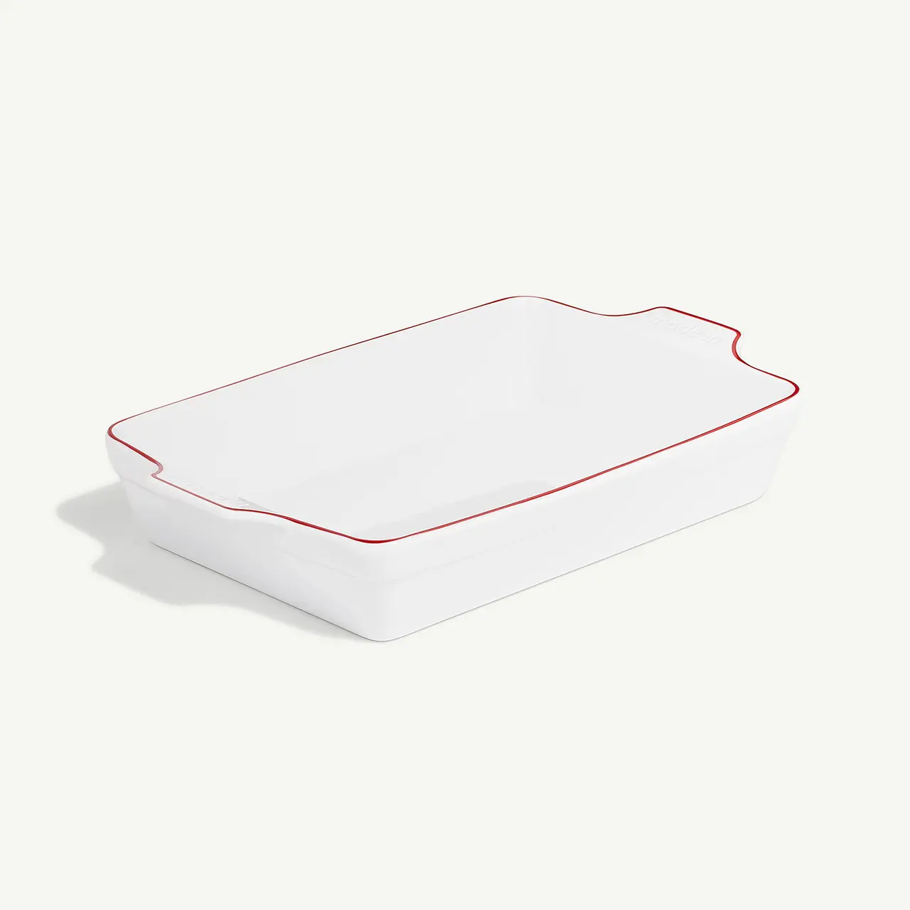 A white ceramic baking dish with red trim on a light background.