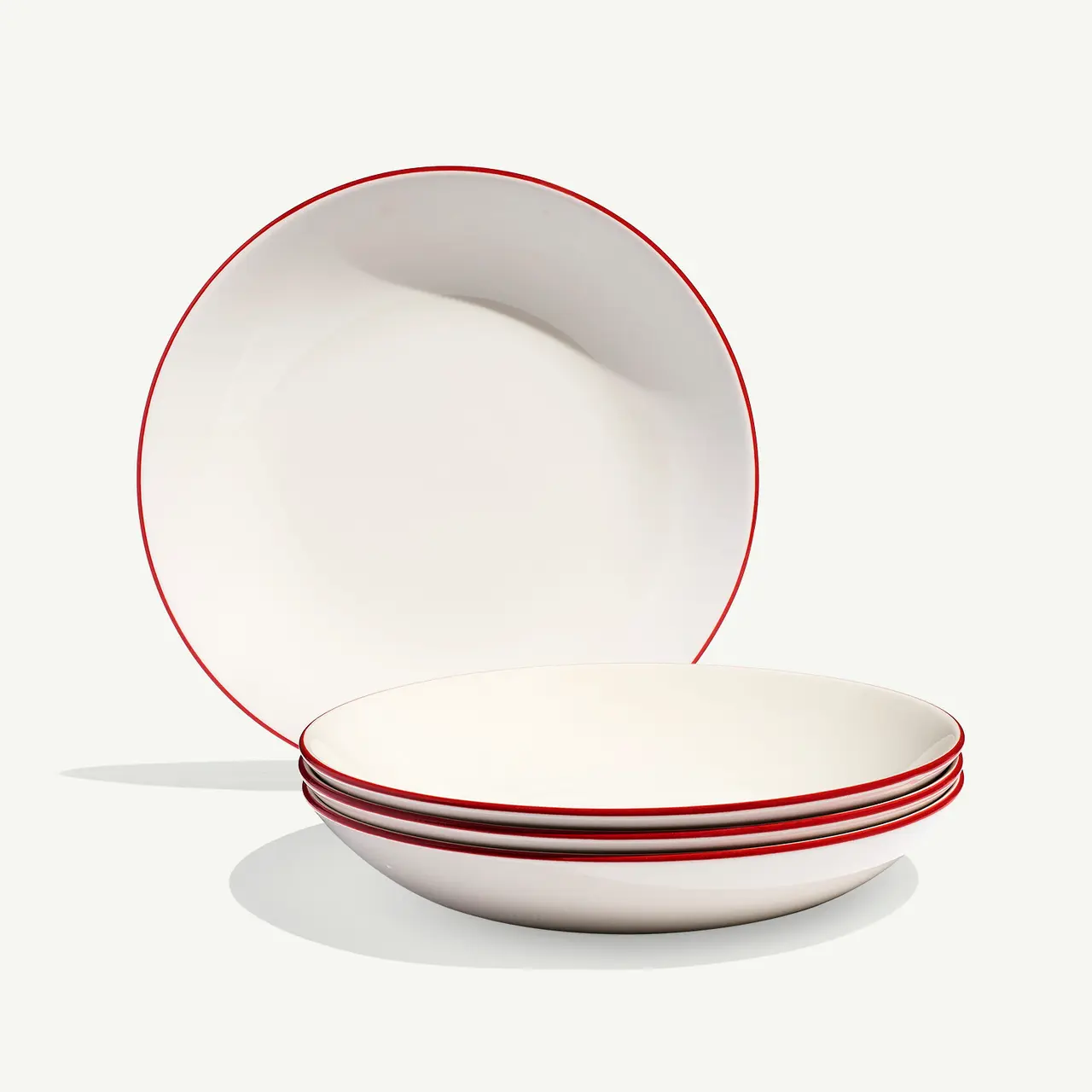 Two white bowls with red trim are stacked with one tilted upright against the other on a light background.