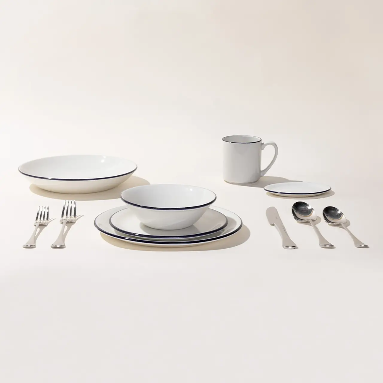 A neatly arranged dinnerware and cutlery set, including plates, bowls, a mug, and silverware, is showcased against a plain background.