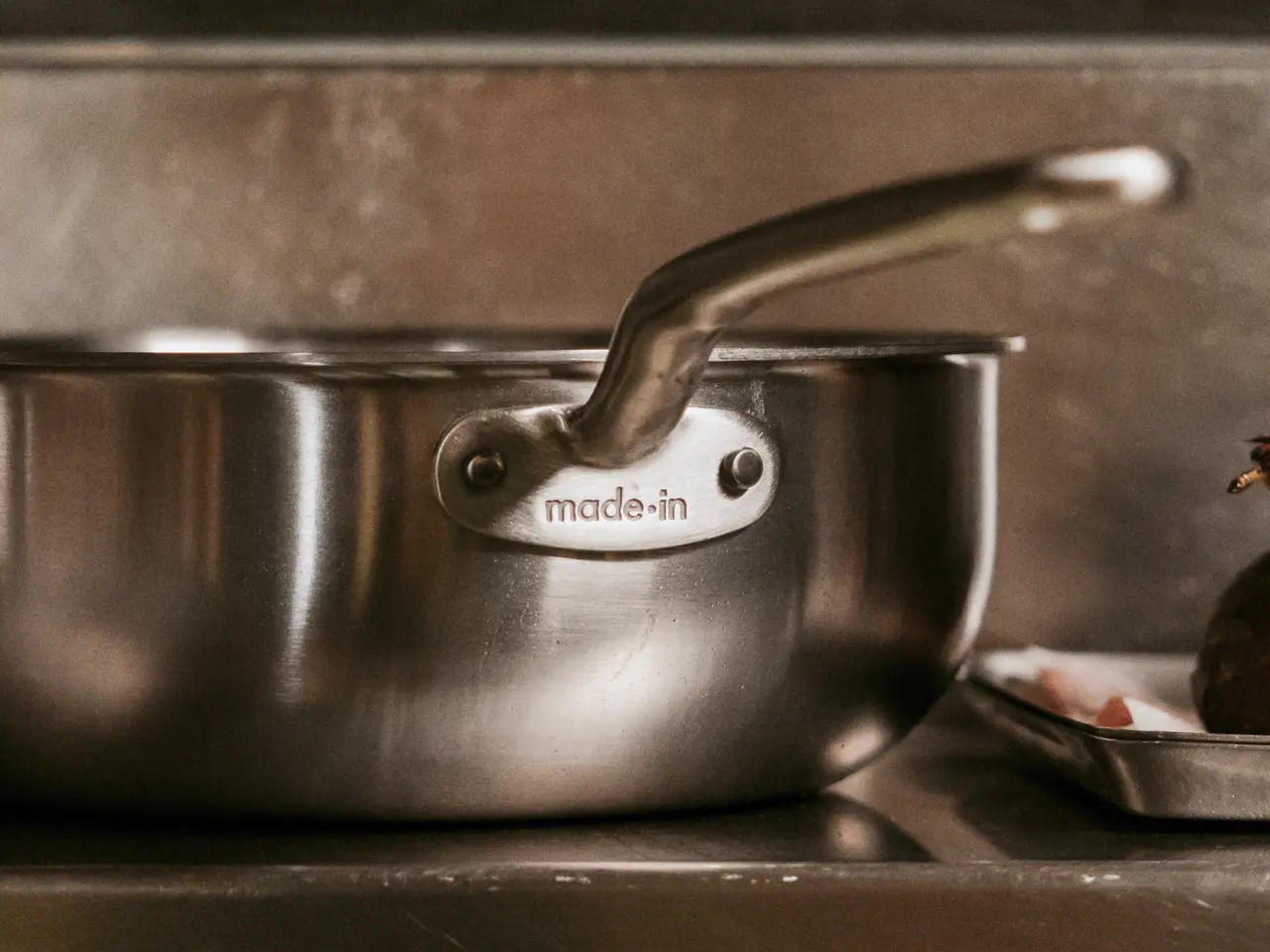 A stainless steel saucepan with a curved handle is resting on a countertop, showcasing the brand logo "made-in" on its side.