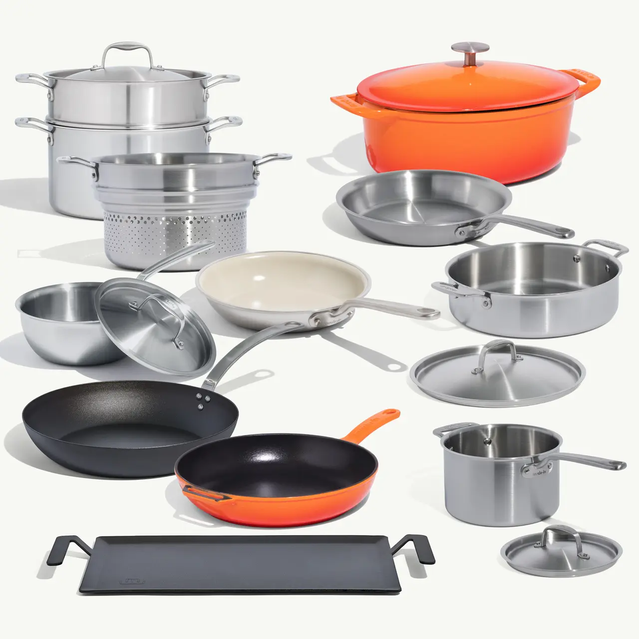 A variety of cookware, including pots, pans, and lids in different colors and materials, is displayed on a light background.