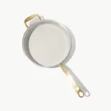 A white pot with a gold handle sits on a light background, showcasing its smooth interior.