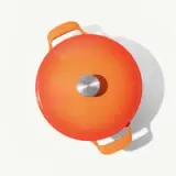 An orange round cooking pot with a silver circular knob on the lid and two handles, captured from above against a light background.