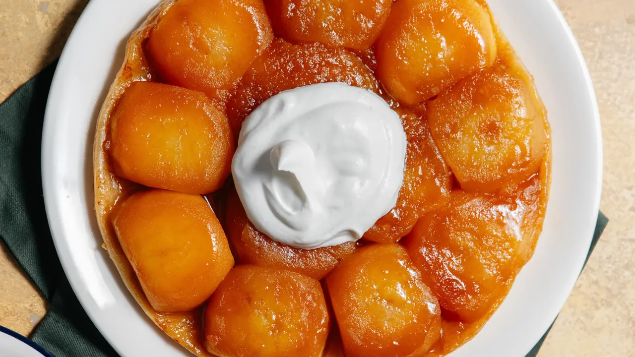 Tarte Tatin topped with caramelized apples and a dollop of whipped cream on a white plate.