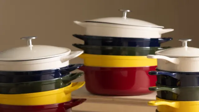 A variety of colorful stacked cookware pots in red, yellow, green, and navy blue with white lids are displayed on a wooden surface.