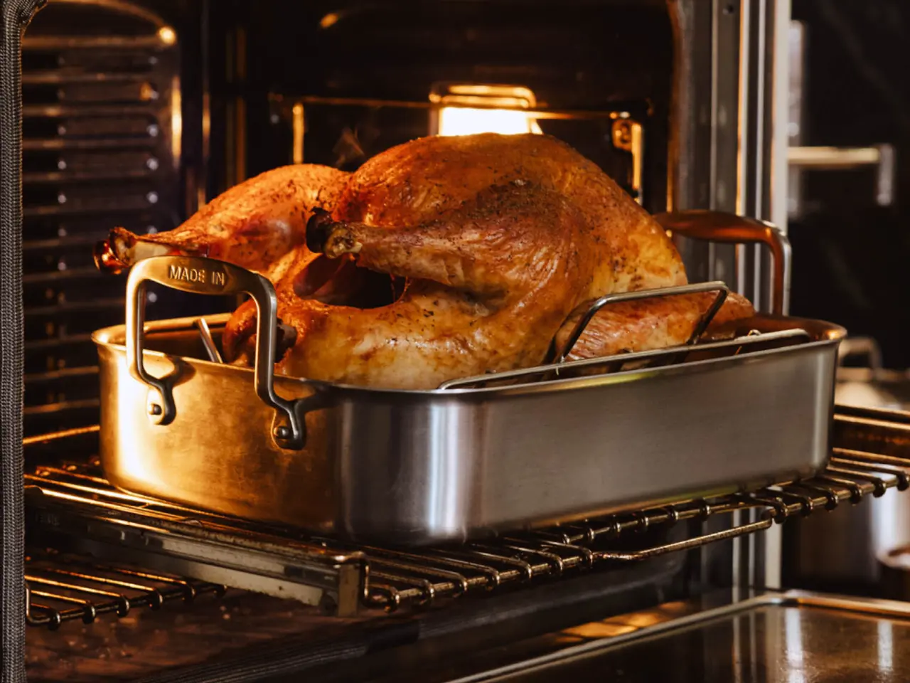 A large, golden-brown turkey is roasting in an oven, nestled in a stainless steel roasting pan.