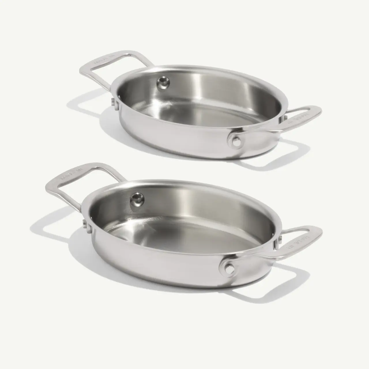 Two shiny stainless steel oval pans are stacked, showcasing their smooth surfaces and handles.