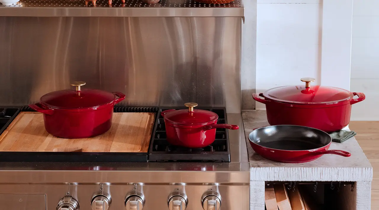 A set of red cookware consisting of pots and a pan on a stainless steel stove in a modern kitchen.