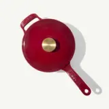 A bright red, enameled cast iron skillet with a brass knob and a long handle.