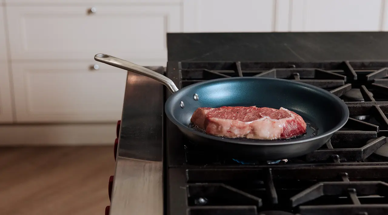 A raw steak with seasoning sits in a pan on a stove top, ready to be cooked.