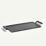A flat griddle with blue handles and a metal spatula, designed for cooking.