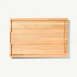 A simple, rectangular wooden cutting board with a visible grain and indented handles on the sides, presented on a plain white background.