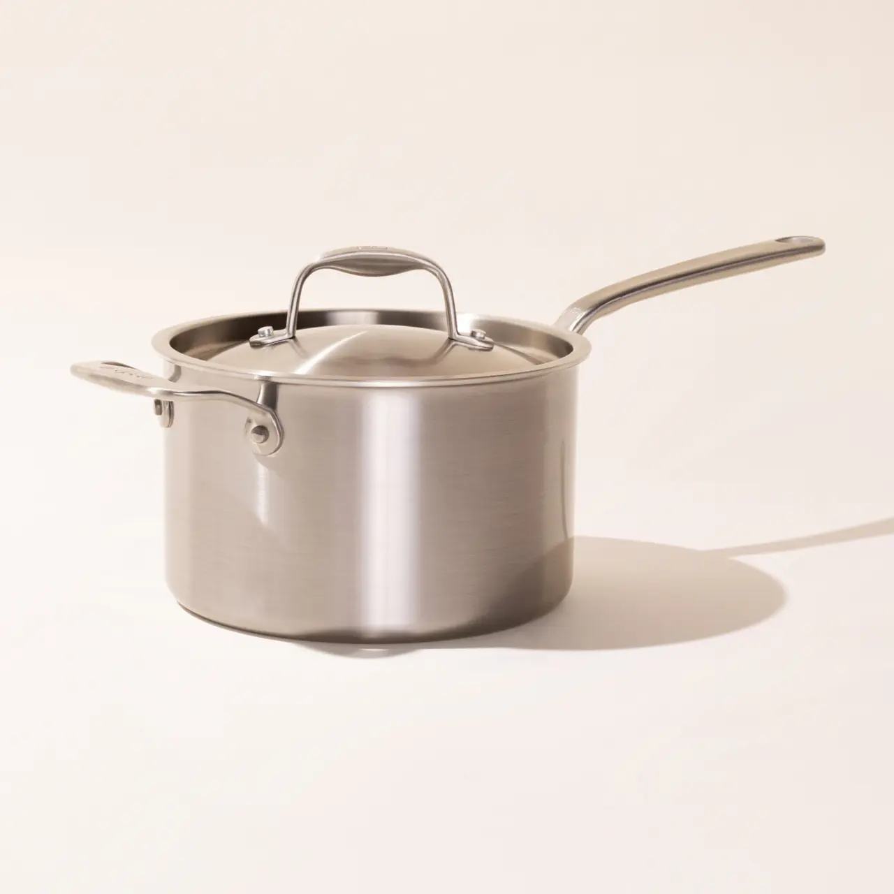 Stainless steel saucepan with a long handle and a lid on a neutral background.