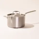 Stainless steel saucepan with a long handle and a lid on a neutral background.