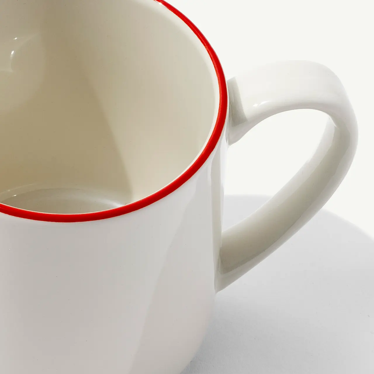 A close-up view of a white mug with a red rim on a white background.