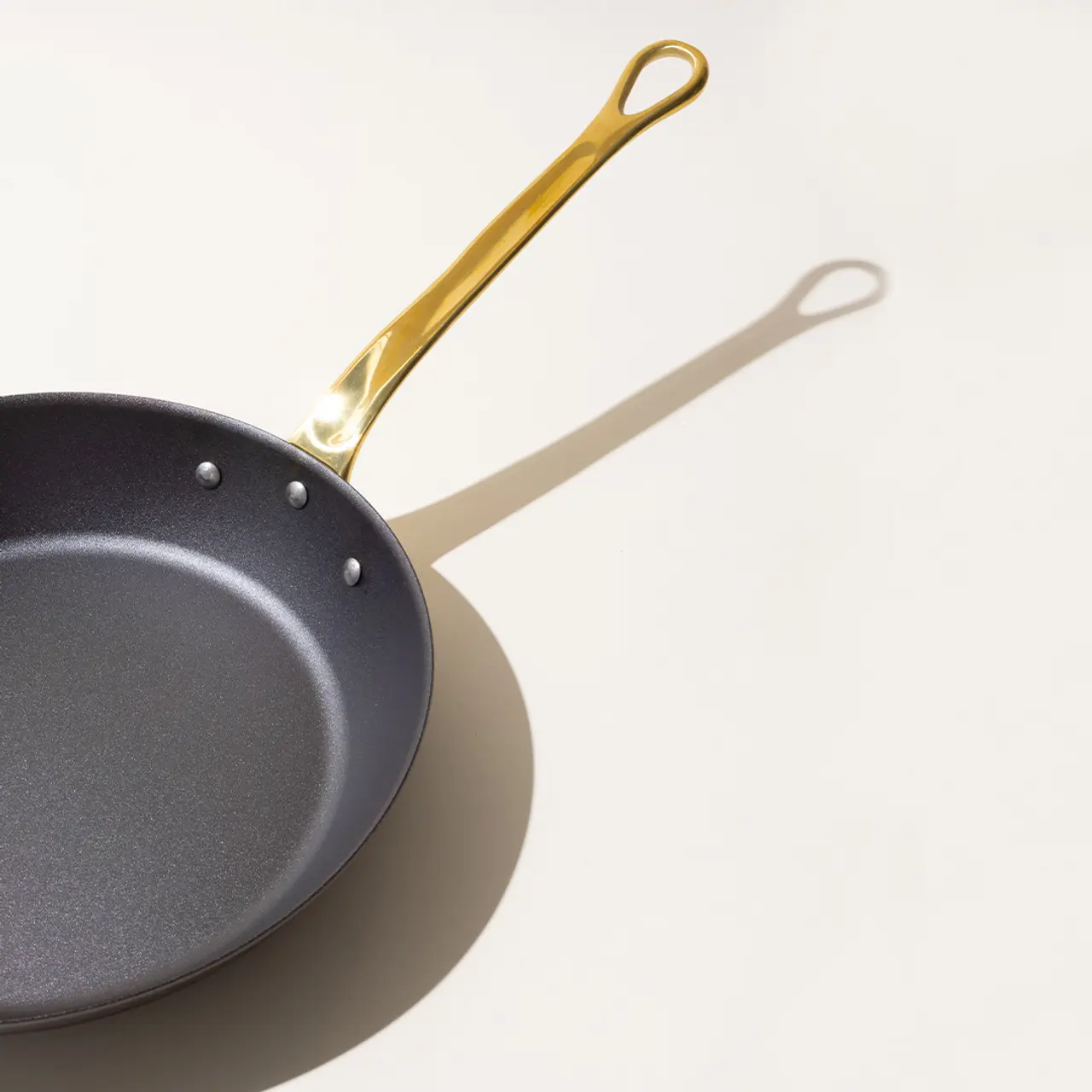 A non-stick frying pan with a golden handle casting a shadow on a light background.