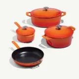 A set of four orange cookware items with various sizes, including a skillet and pots with lids, on a light background.