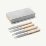 Four kitchen knives with light-colored handles are positioned in front of a silver box that contains them.