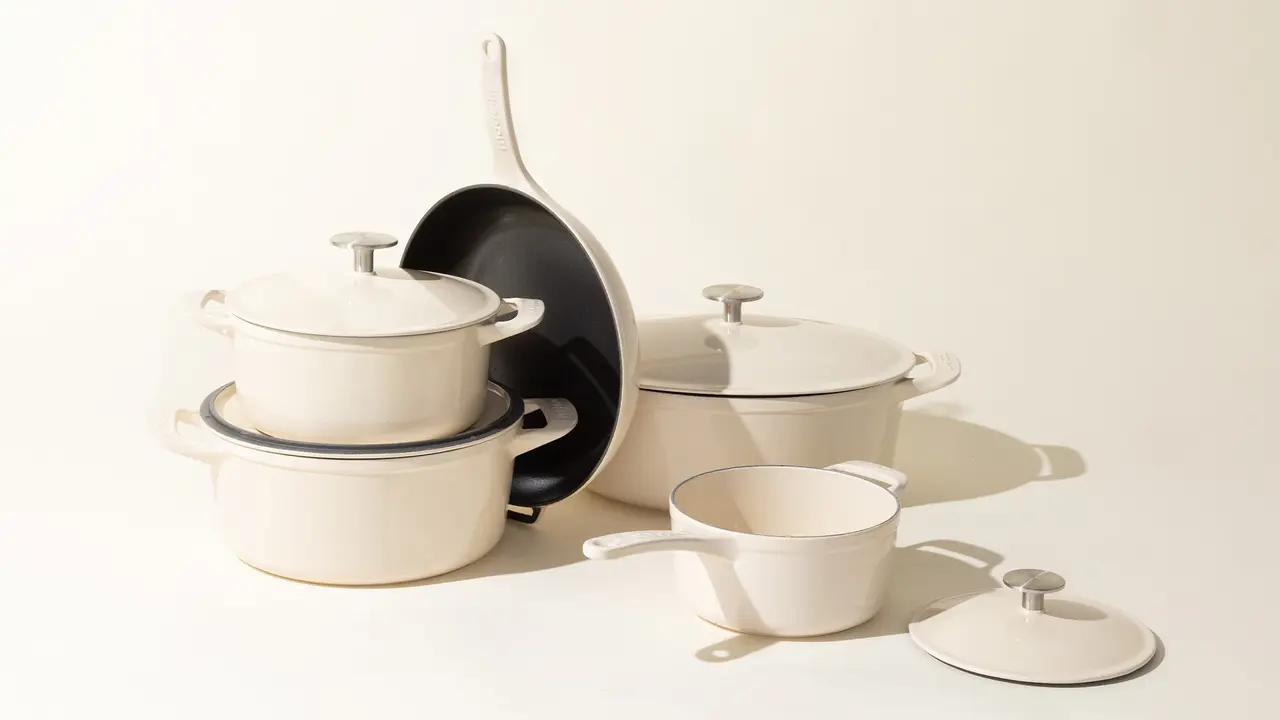 A set of cream-colored kitchen pots and pans with lids neatly stacked and placed against a light background.