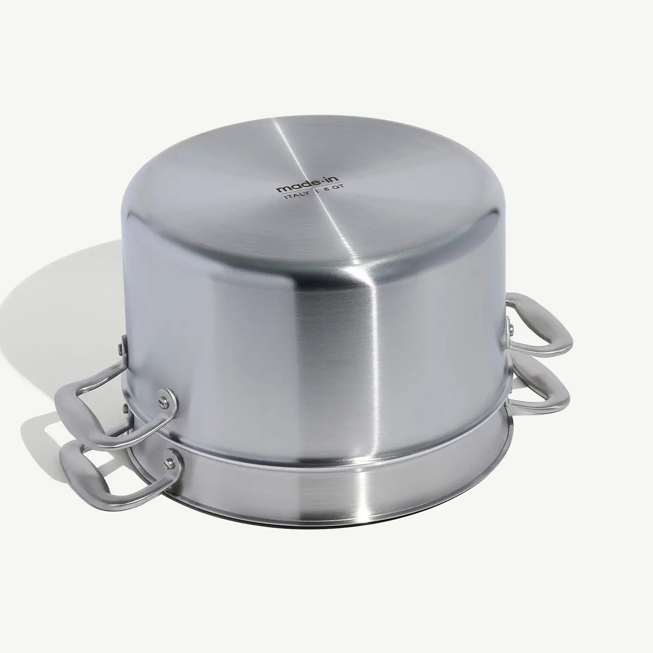 A stainless steel food container with clamps on the side sits on a light surface.
