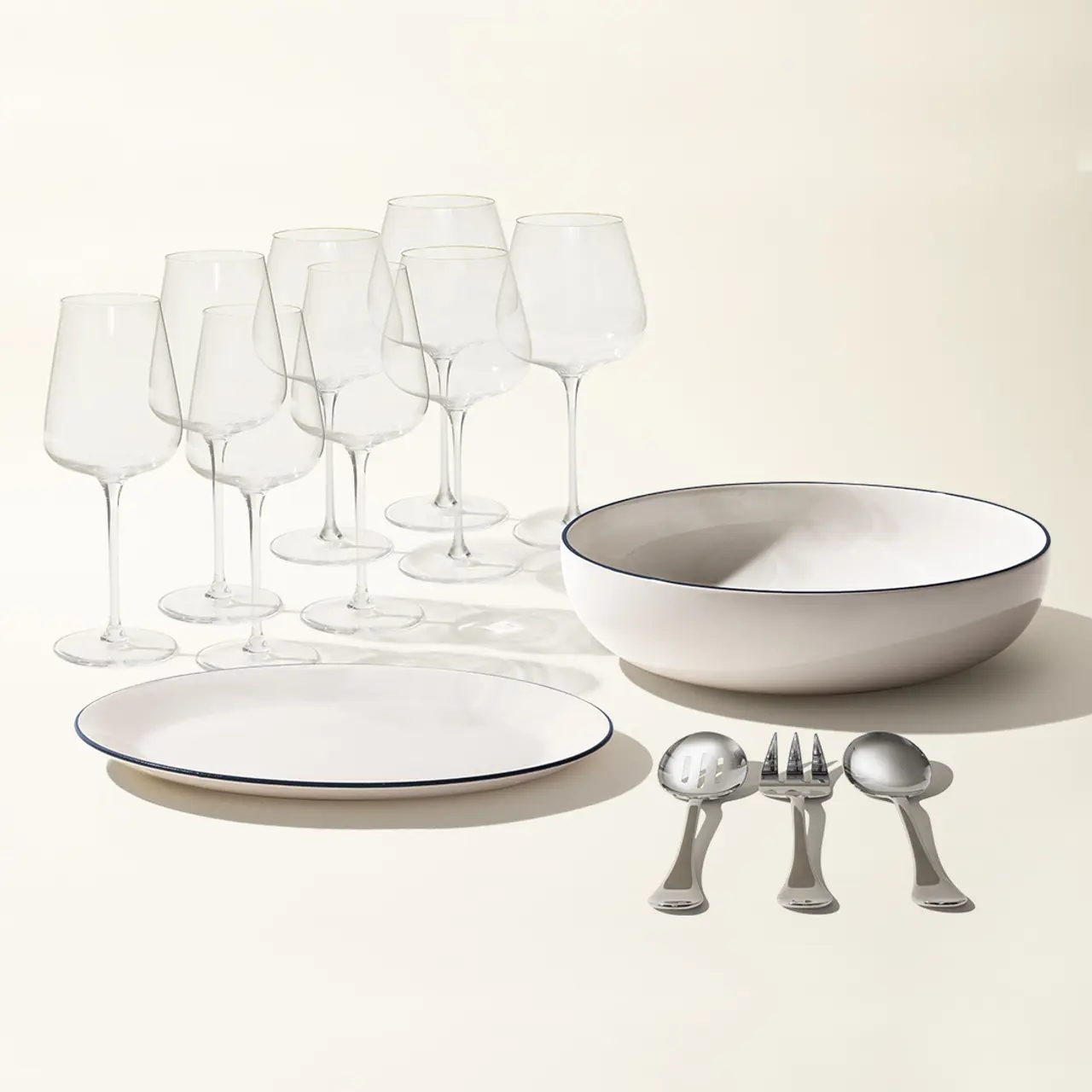 A neatly arranged set of dinnerware and cutlery, featuring plates, a bowl, several wine glasses, and a spoon, fork, and knife, against a light background.