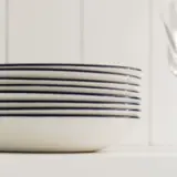 A stack of clean white plates with blue stripes is placed on a white surface next to a blurry fork.
